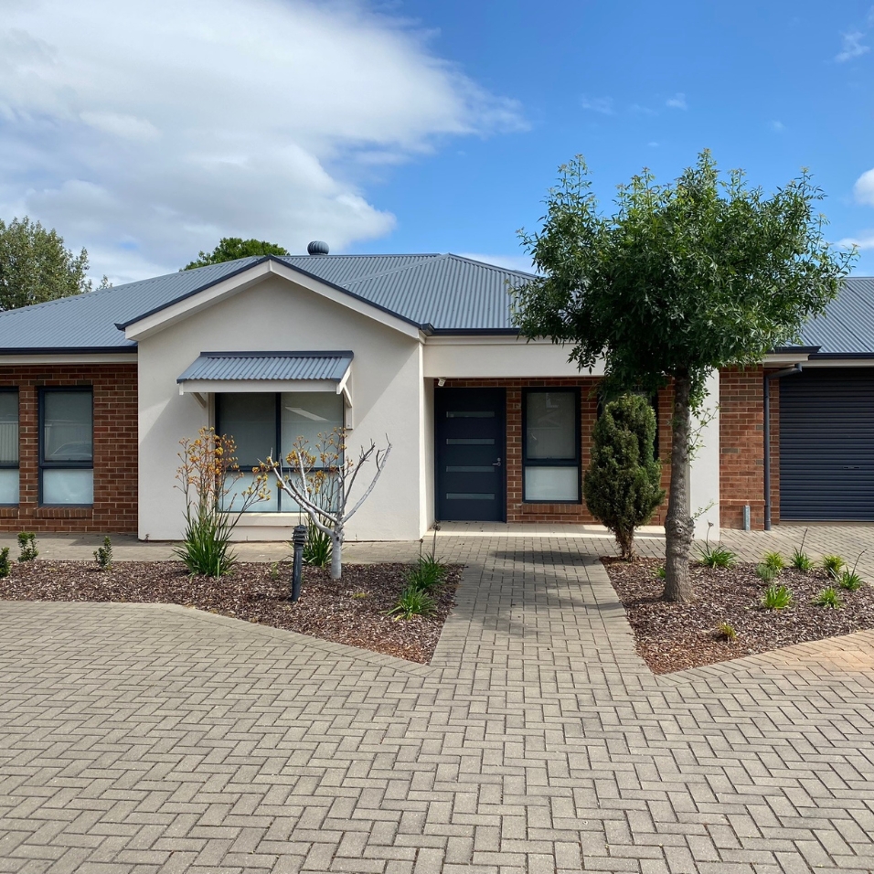 Front view of a red brick home with a cream rendered front. It has a grey corrugated roof with a small garden and landscaped path at the front.