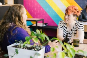 Two people at a cafe table with a rainbow painted wall in the background.