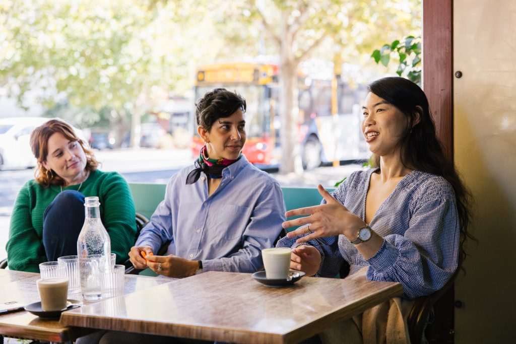 Three people sitting at a cafe table talking.
