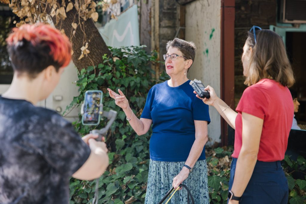 A person using an assistance dog is being interviewed by two people on the street.
