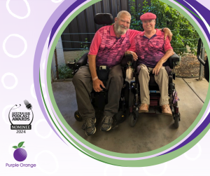 Light putple background with white spots. Photo of Trudy and Chris smiling at the camera wearing pink shirts, an arm around each other. Chris has his arm around Trudy.